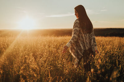 Woman standing on field against sky during sunset