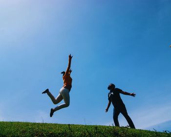 Low angle view of man looking at woman jumping on field against sky