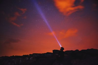 Silhouette man with flashlight against sky at night