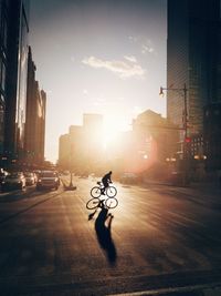Silhouette person cycling on street during sunset