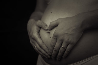 Midsection of pregnant woman touching her belly against black background