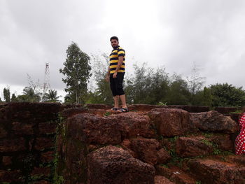 Young man standing by tree against sky