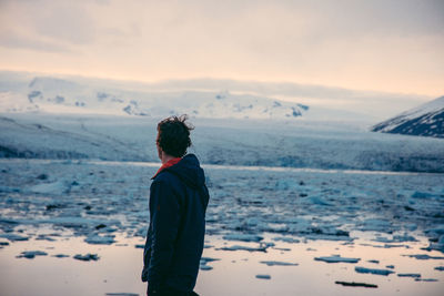 Side view of young man standing by lake during winter