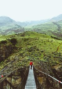 Hiker walking on footbridge by mountains against sky