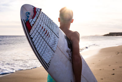 Rear view of boy holding surfboard standing on beach