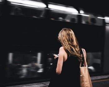 Rear view of woman using mobile phone at railroad station platform