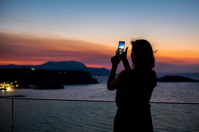 Man photographing using smart phone against sky during sunset