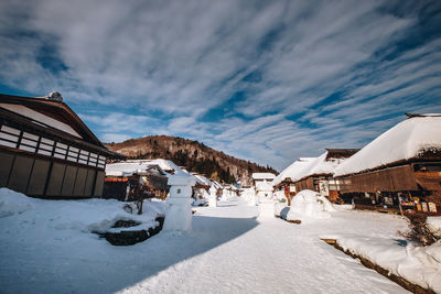 People on snow covered houses by buildings against sky