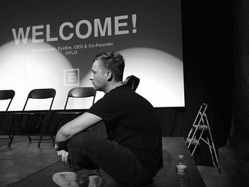 Side view full length of thoughtful man sitting on stage against projection screen