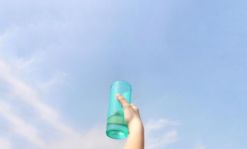 Close-up of hand holding blue ring against sky