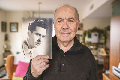 Portrait of senior man showing an old picture of himself