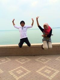 Full length of young couple jumping in sea against sky