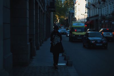 Rear view of man walking on street amidst buildings