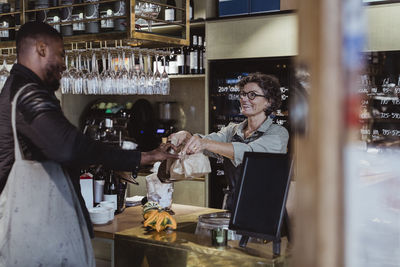 Male customer collecting order from female owner at store