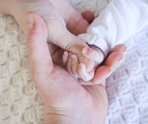 Cropped image of parents holding baby hand on bed