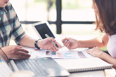 Midsection of business people discussing over graphs at desk