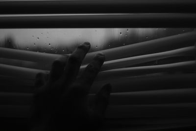 Cropped image of hand touching window blinds during monsoon