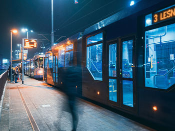 The tram leaves the stop in night city, motion blur view