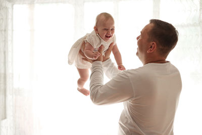 Father and daughter laughing on light window, toddler on hands. happy loving family. father 
