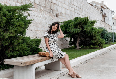 Portrait of attractive young woman in summer polka-dot dress sitting on bench.