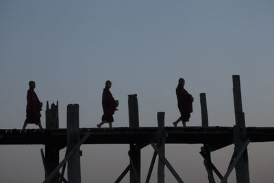 Silhouette monks walking on footbridge against clear sky during sunset