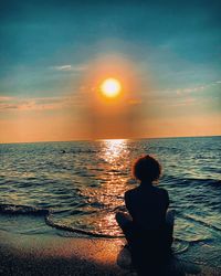 Rear view of woman sitting on sea during sunset