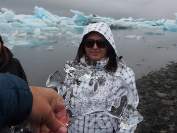 Cropped hand of man holding icicle against woman at beach