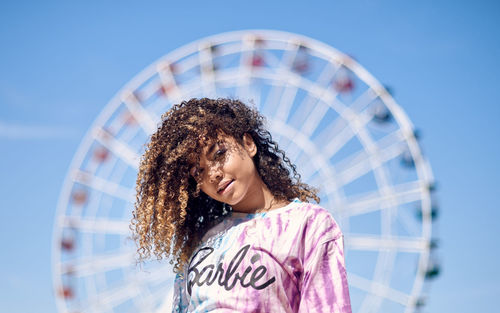 Portrait of beautiful young woman with curly hair against ferris wheel