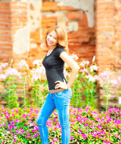 Portrait of smiling woman with hand on hip while standing by flower plants