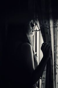 Young woman standing by window in room at home