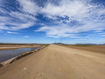 Dirt road amidst land against sky