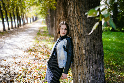 Portrait of young woman standing amidst trees at park