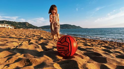 Toddler girl running with a red ball playing football  along the beach 