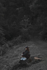 Side view of man sitting on rock in forest