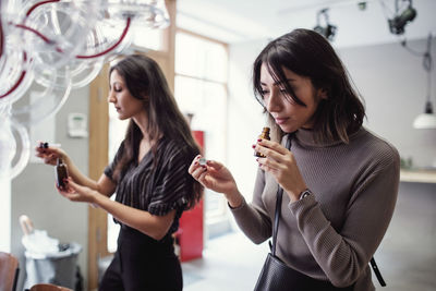 Young multi-ethnic female colleagues smelling perfume bottle while standing at workshop