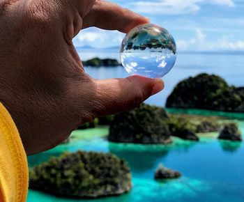 Cropped hand of man holding crystal ball against sky