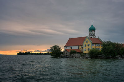 Church by sea against cloudy sky during sunset