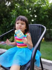 Cute girl eating flavored ice while sitting on chair