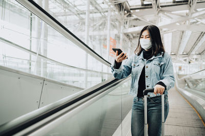 Smiling woman wearing mask using smart phone on escalator