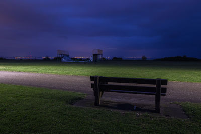 Empty bench on field against sky at dusk