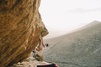 Side view of man rock climbing against sky