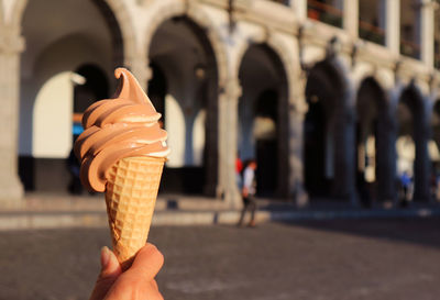 Hand holding a two-tone soft serve ice cream cone, with blurred neoclassical style building