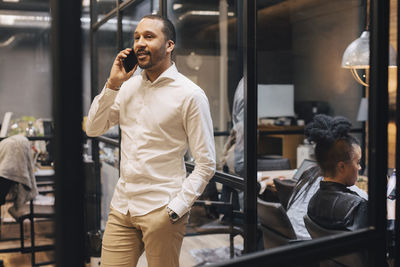 Smiling businessman with hand in pocket talking on mobile phone at office