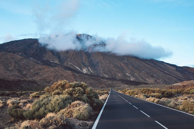 Road leading towards mountains against sky