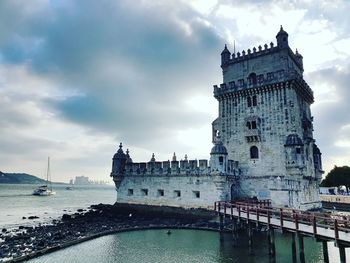 Building by sea against cloudy sky
