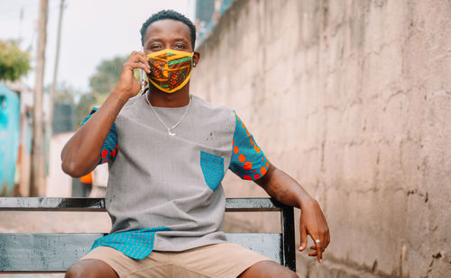 Portrait of man holding camera while standing against wall