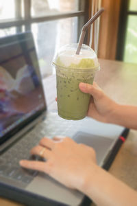 Cropped image of woman using laptop while holding iced matcha latte