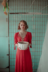 Young woman in red dress holding potted plant while standing at home
