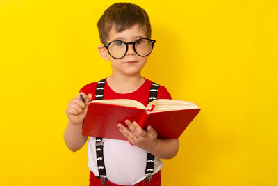 Boy wearing sunglasses standing against yellow background