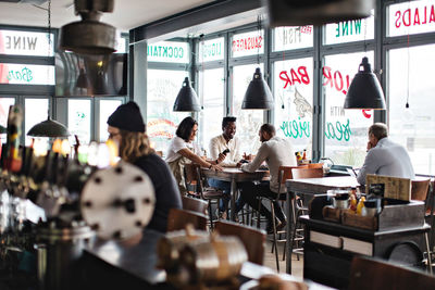 Owner standing by young customers at table in restaurant